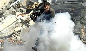 A Palestinian Reuters TV cameraman runs as Israeli troops throw stun grenades at journalists in front on Yasser Arafat's HQ